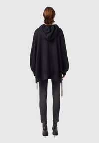 Överdimensionerad svart hoodie med dragsko, med en känguruficka och ribbad fåll, kombinerad med tätsittande grå jeans och svarta ankelstövlar.