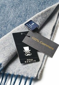 Light blue cashmere scarf with fringed edges; tags stating "100% Cashmere" and brand "Prince Bowtie" are attached, featuring a logo.