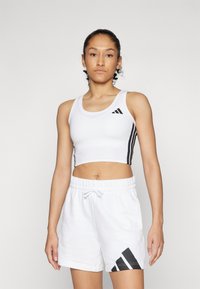 Débardeur de sport blanc avec un design à trois bandes noires et un logo. Associé à un short blanc avec un accent logo noir. Texture lisse.