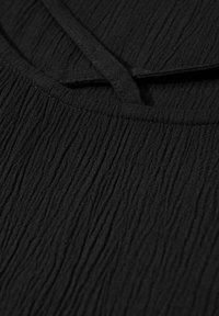 Tessuto nero testurizzato con un leggero effetto stropicciato, con scollatura piatta e dettaglio con lacci regolabili. Nessun motivo o hardware visibili.