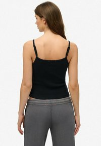 Zwart, aansluitend tanktop met dunne bandjes en ribbeltextuur, gecombineerd met grijze broek met een brede tailleband en rode accenten.