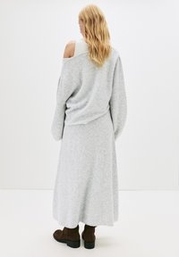 Pulover gri tricotat cu un croi supradimensionat, design off-shoulder, asortat cu o fustă lungă și o pereche de cizme brown până la gleznă cu toc gros.