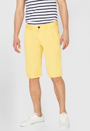 Gele katoenen shorts met een rechte snit, voorzakken en een knoopsluiting, gecombineerd met een gestreept shirt en witte sneakers.