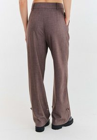 Hnedé nohavice s širokými nohavicami z textúrovanej látky. Sú vybavené detailom gombíka na leme a bočnými vreckami. Dokončené čistým pásom.