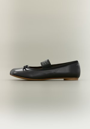 Ballerina in pelle nera con piccolo fiocco sulla punta, cinturino elastico con logo sulla parte superiore e tacco basso in legno, vista laterale.