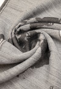 Tessuto grigio testurizzato con un motivo a rotolo, caratterizzato da motivi astratti più scuri e cuciture visibili lungo i bordi. Morbido e leggero.