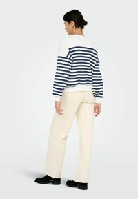 Marinblå och vit randig sweatshirt med avslappnad passform, långa ärmar och ribbad mudd. I kombination med krämfärgade vida byxor och svarta ankelstövlar.