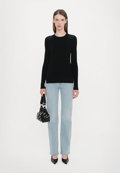 Black ribbed long-sleeve top with shoulder details, paired with light blue straight-leg jeans and a small black handbag with accents.
