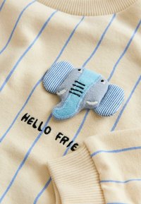 Béžový svetr s modrými pruhy, s aplikací slona v modré a šedé barvě a vyšitým nápisem "HELLO FRIEND" černou barvou.