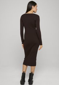 Robe midi marron côtelée à manches longues et encolure carrée, avec une silhouette ajustée. Associée à des bottines noires.
