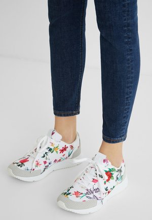 Zapatillas blancas con estampado floral multicolor y detalles grises, usadas con vaqueros ajustados azul oscuro que terminan por encima del tobillo.