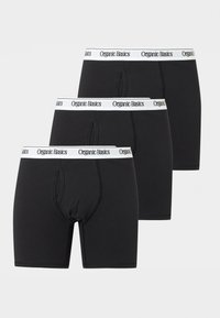 Τρία μαύρα ανδρικά εσώρουχα μποξεράκια με λευκές ελαστικές ζώνες στη μέση που γράφουν "Organic Basics", στοιβαγμένα σε μετατοπισμένη διάταξη.
