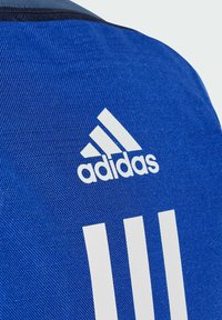 Textil azul con un acabado texturizado. Presenta un logo de Adidas en blanco y tres franjas verticales en blanco. El diseño es deportivo y funcional.