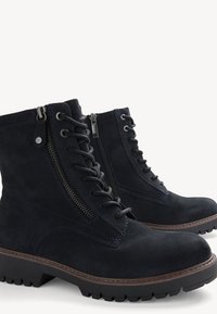 Bottines en daim noir à lacets avec fermetures éclair latérales, bouts ronds, semelles épaisses à crampons, et couture marron le long des bords des semelles.