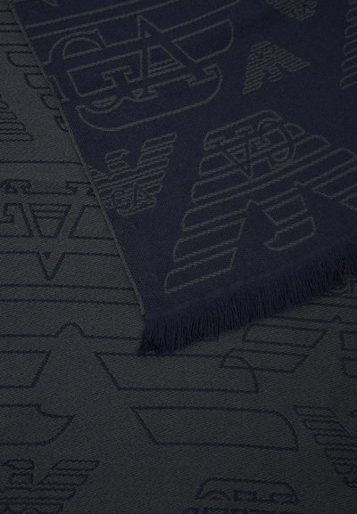 Tissu foncé avec des formes géométriques abstraites et ailées en relief, comprenant un bord avec franges sur la pièce supérieure.