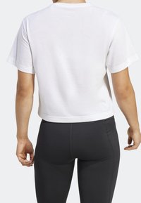 Camiseta corta de algodón blanco con mangas cortas, cuello redondo y textura suave, combinada con leggings negros de cintura alta.