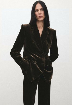 Blazer de terciopelo marrón oscuro de doble botonadura con solapas amplias, botones grandes y un corte estructurado. Textura suave, combinado con pantalones a juego.