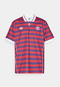 Czerwono-niebieski piłkarski garnitur w wzór rombów z białym kołnierzykiem, z logo i oznakowaniem na klatce piersiowej i rękawach.