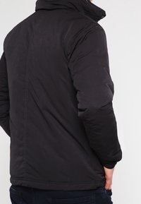 Czarna pikowana kurtka z wysokim kołnierzem, o gładkiej powierzchni, miękkiej teksturze i kontrastowym przeszyciu. Model o średniej długości, bez widocznych logo.