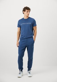 Μπλε βαμβακερό T-shirt με το "BJÖRN BORG" τυπωμένο σε λευκό, συνδυασμένο με αντίστοιχες μπλε φόρμες που διαθέτουν ένα διακριτικό λογότυπο. Λευκά αθλητικά παπούτσια.