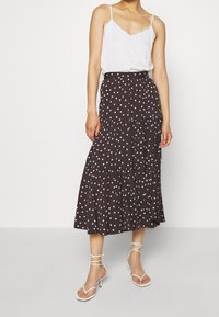 Bruine midi-rok in lagen met witte stippen en een elastische tailleband. Gecombineerd met een witte top en witte sandaalhakken met bandjes.