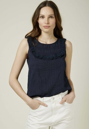 Haut sans manches bleu marine en tissu texturé avec une volute en dentelle décorative le long de l'encolure, associé à un pantalon blanc.