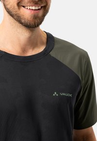 Camiseta de manga corta en negro y verde con tejido texturizado, cuello redondo y logotipo de VAUDE en verde. Presenta paneles de hombro contrastantes.