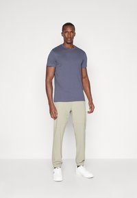 Marineblå t-skjorte med korte ermer, sammen med lysebeige joggebukser. Buksene har elastiske mansjetter og en jevn tekstur. Hvite joggesko fullfører antrekket.