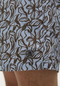 Shorts de bain en tissu bleu clair avec des motifs floraux bruns. Comprend un bouton noir circulaire avec un design de crâne.