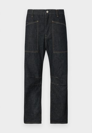 Mørk denimbukser med lige snit, der har to store forlommer foran og kontrastfulde gule syninger langs sømmene.