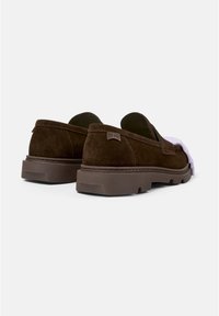 Braune Wildleder-Slipper mit einer dicken braunen Gummisohle, die ein dezentes Etikett an der Ferse und ein glattes Innenfutter aufweisen.