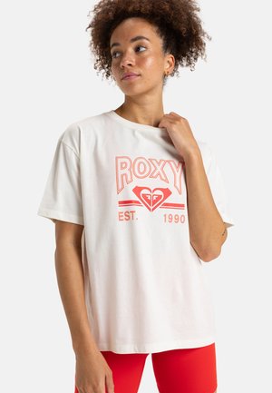 T-shirt en coton blanc à manches courtes, arborant un graphique coral audacieux "ROXY" et un logo de cœur, avec "EST. 1990" en dessous.