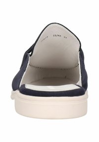 Marinblå mockasinsko utan snörning med vit gummisula och öppen bak. Inuti finns en slät foder. Minimalistisk design utan synlig logga.