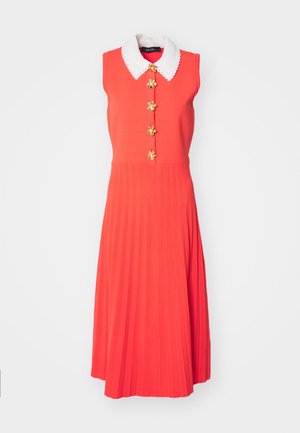 Robe sans manches rouge avec un col blanc en forme de scallop, ornée de boutons floraux dorés et d'un design de jupe plissée.