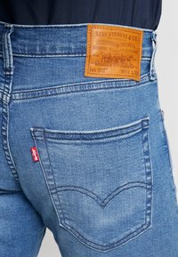 Ljusblå denimjeans med en läderpatch på baksidan märkt "Levi Strauss & Co." och en röd etikett på vänster bakficka. Har klassisk sömnad.