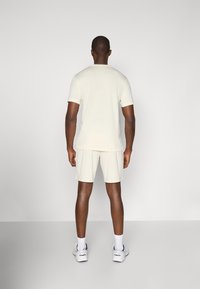 Set di tshirt a maniche corte e pantaloni corti color beige chiaro, realizzato in materiale morbido, con una vestibilità casual. Scarpe da ginnastica bianche indossate con calzini bianchi.