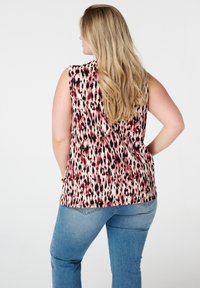 Top sans manches avec un motif abstrait multicolore affichant des nuances de rose, de noir et de blanc ; associé à un jean en denim bleu clair.