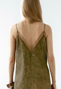 Olive green slip dress with a V-shaped back, sheer straps, and a soft, textured fabric, featuring an irregular pattern.