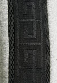 Primer plano de una tira de tela negra con un patrón geométrico texturizado rodeada de malla negra sobre un fondo textil gris.