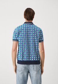 Kortärmad pikétröja med ett geometriskt mönster i blått, grönt och vitt. Ribbad krage och muddar, med en enfärgad marinblå fåll.