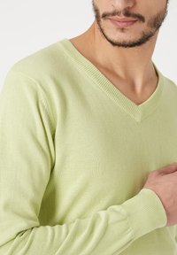 Jersey verde claro en forma de V, fabricado en un suave tejido de punto, con bordes acanalados en el escote y los puños, y con una silueta ajustada.