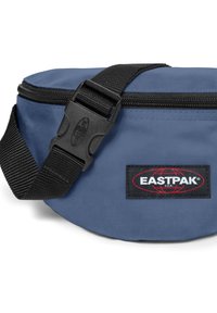 Borsa a tracolla rotonda in tessuto blu con una superficie liscia, cintura nera regolabile e una fibbia di rilascio laterale. Presenta un patch logo Eastpak.