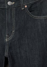 Close-up van donkerblauwe spijkerbroek met zicht op voorvak, knoop, riemlus en beige stiksel details.