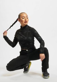 Fekete, hosszú ujjú, diszkrét paisley mintás top, cropped fazonban, fekete nadrággal és sárga akcentusokkal ellátott, vastag talpú sportcipőkkel párosítva.
