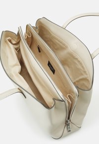 Sac à main en cuir beige texturé avec une fermeture éclair, une doublure intérieure lisse et plusieurs compartiments pour l'organisation.