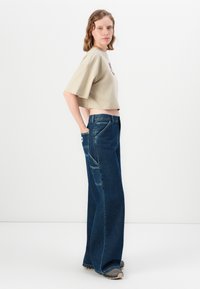 En avskåret beige T-skjorte med korte ermer; kombinert med løstsittende, mørkeblå denimjeans med lommer på siden og rett ben-design.