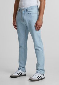 Heledad hall denim teksad, millel on sirge lõige, ees taskud, lukuga esitasku ja brändi nupp. Kombineeritud mustade ja valgete spordijalatsitega.