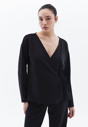 Top noir en tissu lisse, avec un décolleté en V profond, des manches longues et un accent de nœud à la taille pour un ajustement ajustable.