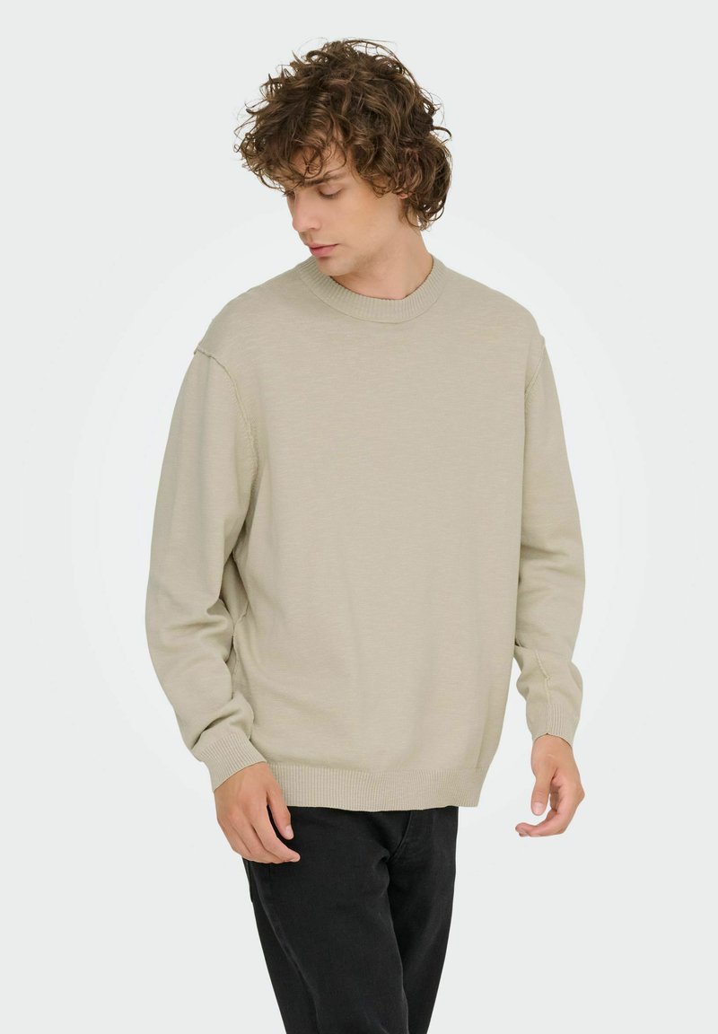 Lichtbeige trui met een ronde hals, lange mouwen en geribde manchetten, gestyled met zwarte broek, met een zachte textuur.