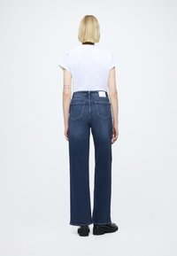 Τζιν παντελόνια με φαρδιά παντελόνα σε σκούρο μπλε, με ψηλή μέση, ολοκληρωμένα με πίσω τσέπες και ραμμένη ετικέτα στη μέση. Στυλιζαρισμένα με λευκό t-shirt.